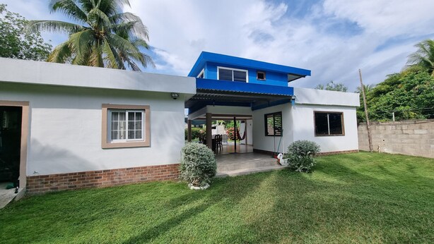 A two-story house with a blue roof and white walls, a covered patio, and a well-maintained lawn.