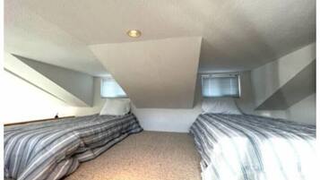 A small attic bedroom with two beds, a sloped ceiling, and a single window.