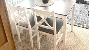 A dining area with a table and chairs, a vase with flowers, and a view through the window. - The Lighthouse Cabin #60 (Gold Beach)