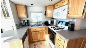 A kitchen with wooden cabinets, a stove, a microwave, and a sink. - The Lighthouse Cabin #60 (Gold Beach)