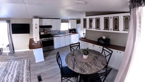 A modern kitchen with white cabinets, a central island, and a dining area with a round table and chairs. - Della’s Delight- Sleeps 4 (Campbellsville)