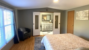 A bedroom with a large bed, a desk, and a bathroom visible through an open door. - Della’s Delight- Sleeps 4 (Campbellsville)