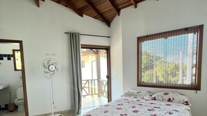 Un dormitorio con cama, ventilador, ventana con persianas y puerta que da al exterior.