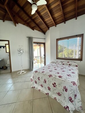 Quarto com cama, ventilador, janela com persianas e porta para o exterior.