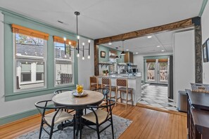 A dining area with a round table, chairs, and a fruit bowl. There is a kitchen area with a counter and appliances. The room has wooden flooring and a checkered floor pattern. - Carolina Cargo at The Cargo Dist. (Wilmington)