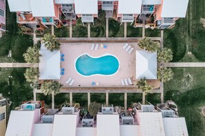 Ein Luftbild eines Hotels mit einem zentral gelegenen Schwimmbecken, umgeben von Liegestühlen und Palmen.