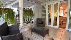 A covered patio area with wicker furniture, a glass-top table, and potted plants.