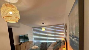 A bedroom with a bed, bedside lamp, and a large window with blinds.