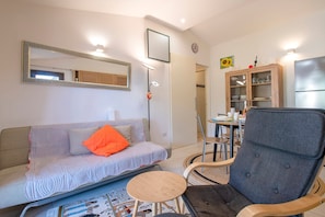 Una sala de estar con sofá, sillón, mesa, aparador y refrigerador.