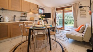 A modern kitchen with wooden cabinets, a dining table with chairs, a TV, and a sofa with a view to the outdoors. - Holiday Home 'Manessy' with Sea View, Shared Pool and Air Conditioning (Badesi)