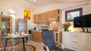 A modern kitchen with wooden cabinets, a built-in oven, a dining table with chairs, and a TV. - Holiday Home 'Manessy' with Sea View, Shared Pool and Air Conditioning (Badesi)
