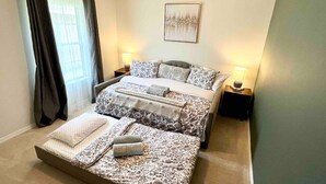 Een slaapkamer met een bed, twee nachtkastjes, een raam met gordijnen en een wanddecoratie.