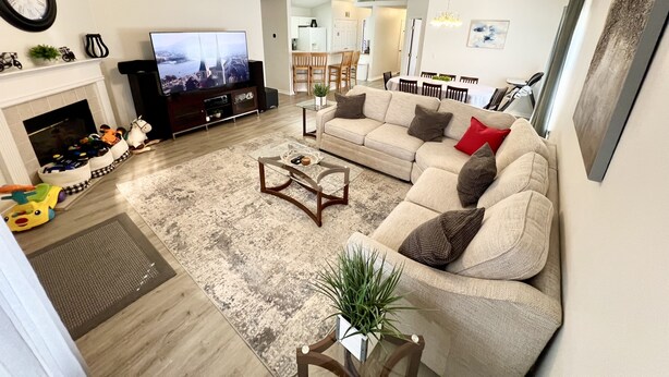 Een woonkamer met een bank, salontafel, televisie, open haard en een eethoek op de achtergrond.
