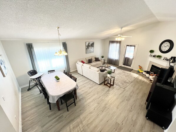 Un salon moderne comprenant un coin repas, un ensemble de canapés, une cheminée et une horloge murale.