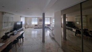 Uma sala de estar ampla com uma televisão grande, assentos e uma área de refeições.