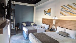 Habitación de hotel con dos camas, ventilador de techo, cabecero de madera, mesita de noche con teléfono y una obra de arte colgada en la pared.