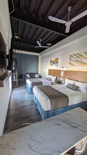 A hotel room with two beds, a ceiling fan, a wooden headboard, a nightstand with a phone, and a wall-mounted artwork. - stay home hotel (Ensenada)