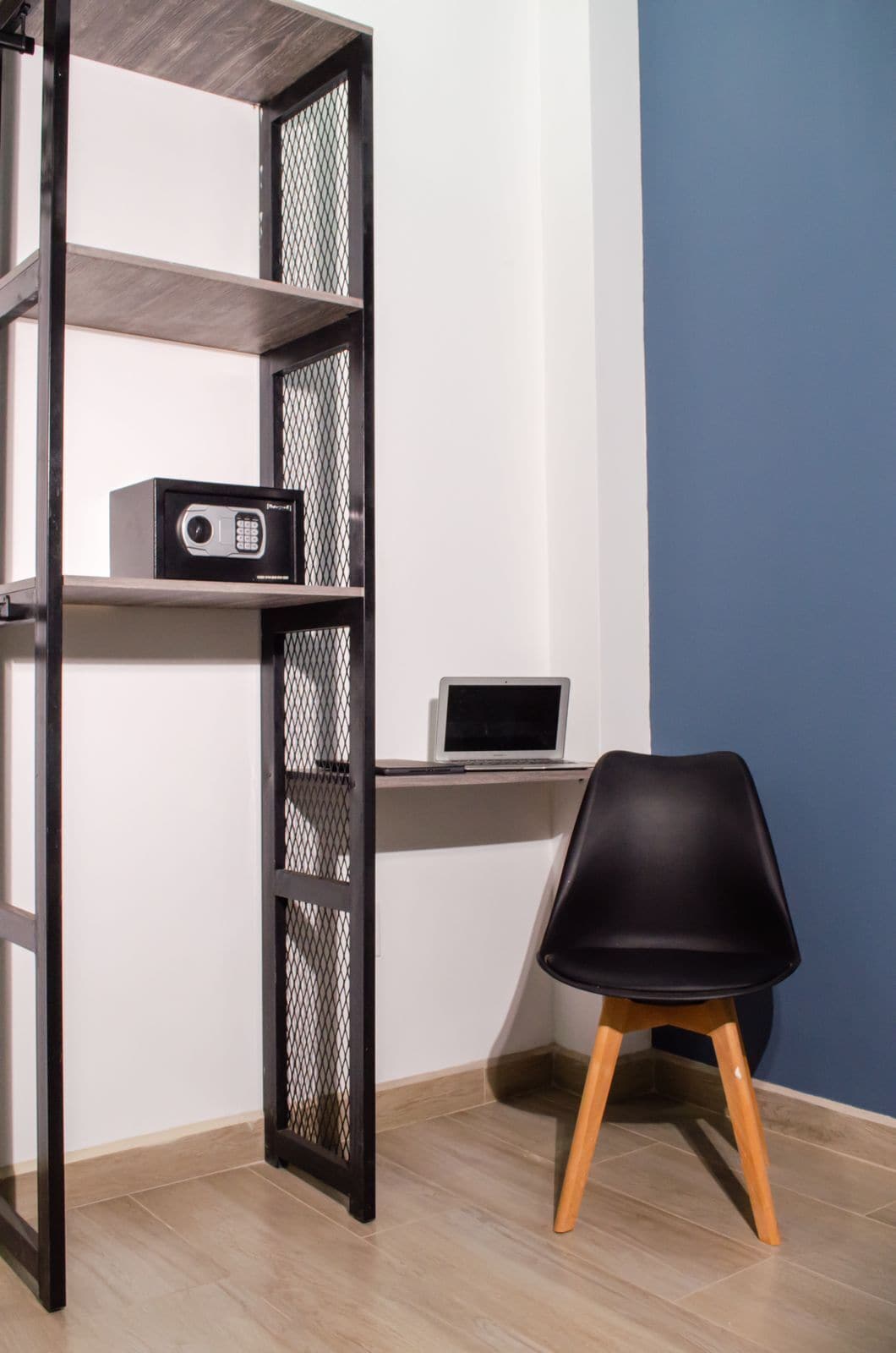 A room with a desk, a chair, a shelf with a radio, and a mesh partition.