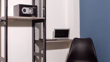 A room with a desk, a chair, a shelf with a radio, and a mesh partition.