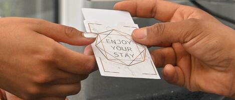A hand holding a card with the text "ENJOY YOUR STAY" and a towel with the logo "STAY HOME HOTEL".
