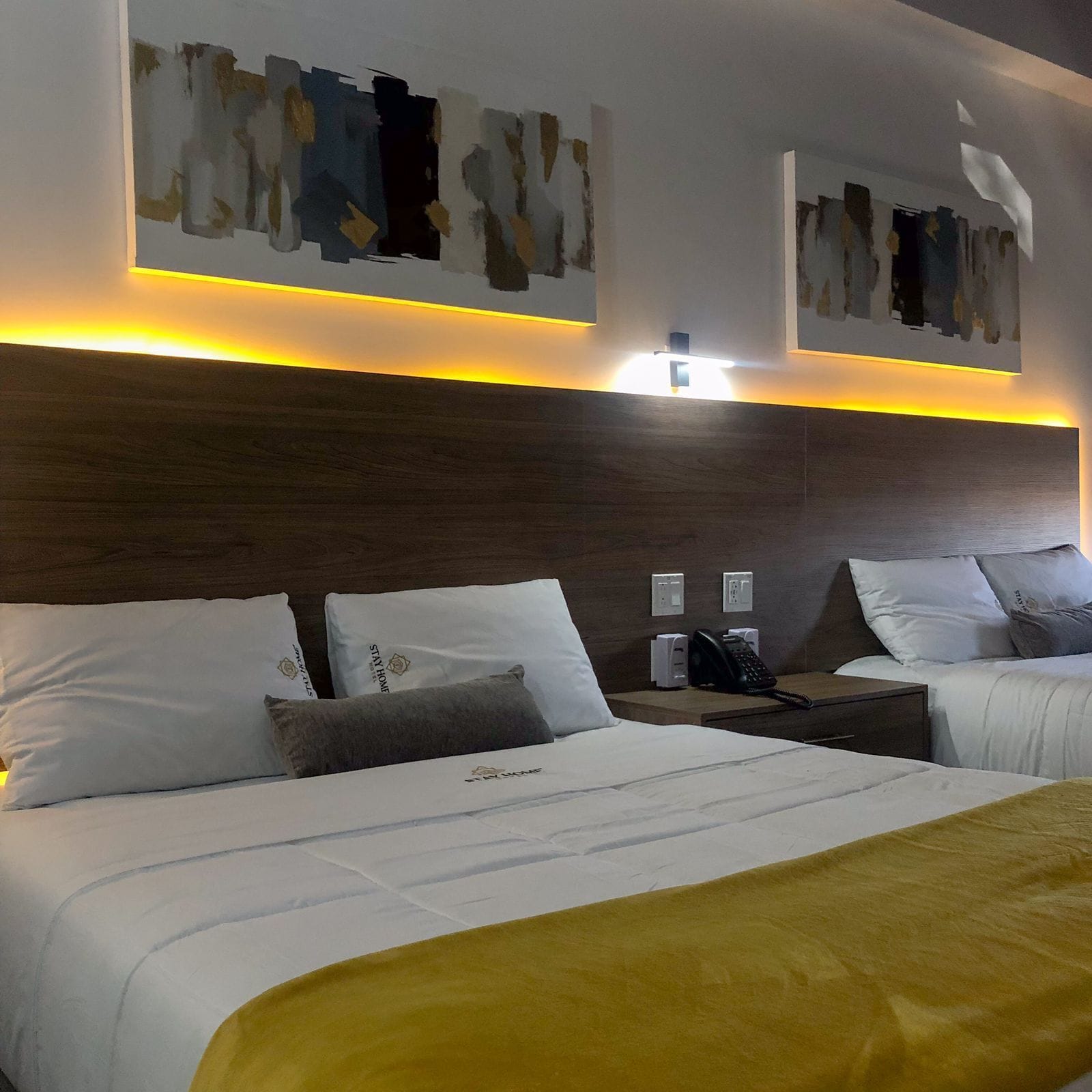 A hotel room with two beds, a wooden headboard, and abstract wall art.