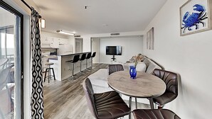 A modern kitchen with white cabinets, a dining area with a round table and leather chairs, and a large window with patterned curtains. - Oceanfront 2B/2B family sized condo (Myrtle Beach)