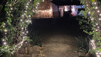 Un sendero al aire libre que lleva a un edificio, rodeado de follaje e iluminado con luces colgantes.