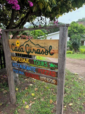 Une enseigne en bois sur laquelle est inscrit « Casa Girasol », et qui indique les services proposés, tels que « HÉBERGEMENT », « EXCURSIONS », « RESTAURANT », « PIZZERIA » et « PISCINE ».