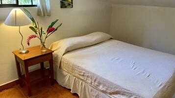 A neatly made bed with a white bedspread in a room with a wooden nightstand holding a lamp and a vase with flowers.