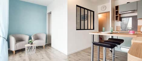 Uma sala de estar moderna com dois poltronas, uma mesinha lateral e um espaço bar com banquetas.