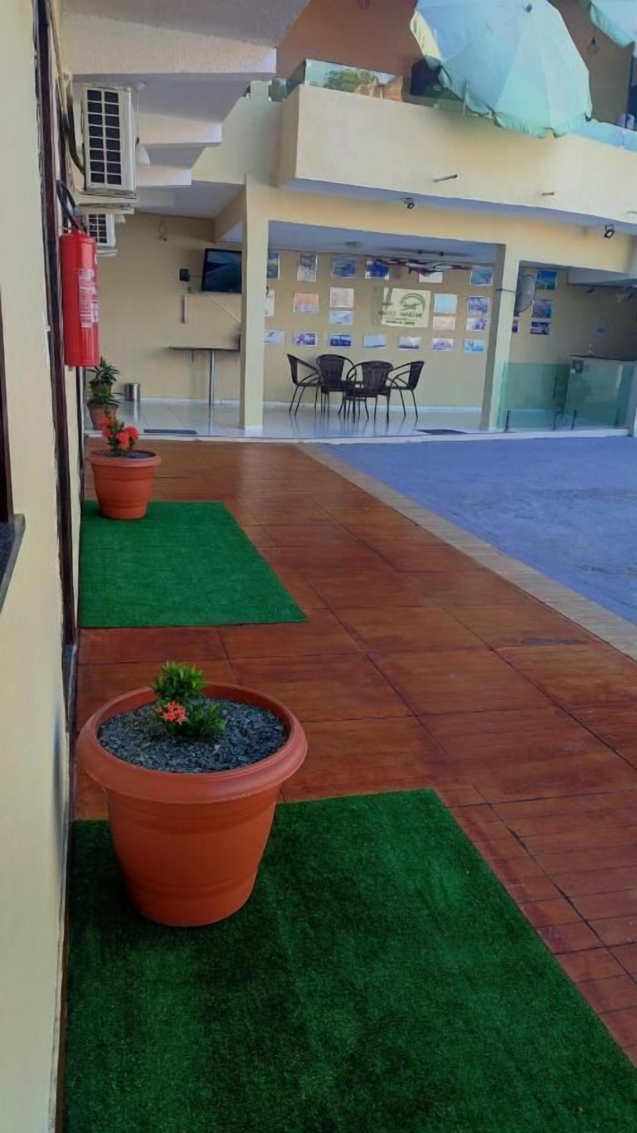 Un couloir d’hôtel agrémenté de plantes en pot, d’un extincteur et d’un espace détente avec des chaises et des tables.