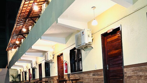 Um saguão de hotel com piso de madeira, plantas em vasos, um extintor de incêndio e um ventilador de teto.