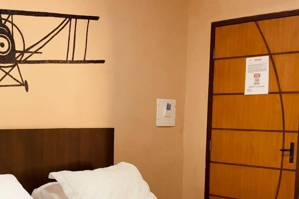 Une chambre d’hôtel avec un lit, des oreillers, une couverture marron et un interrupteur fixé au mur.