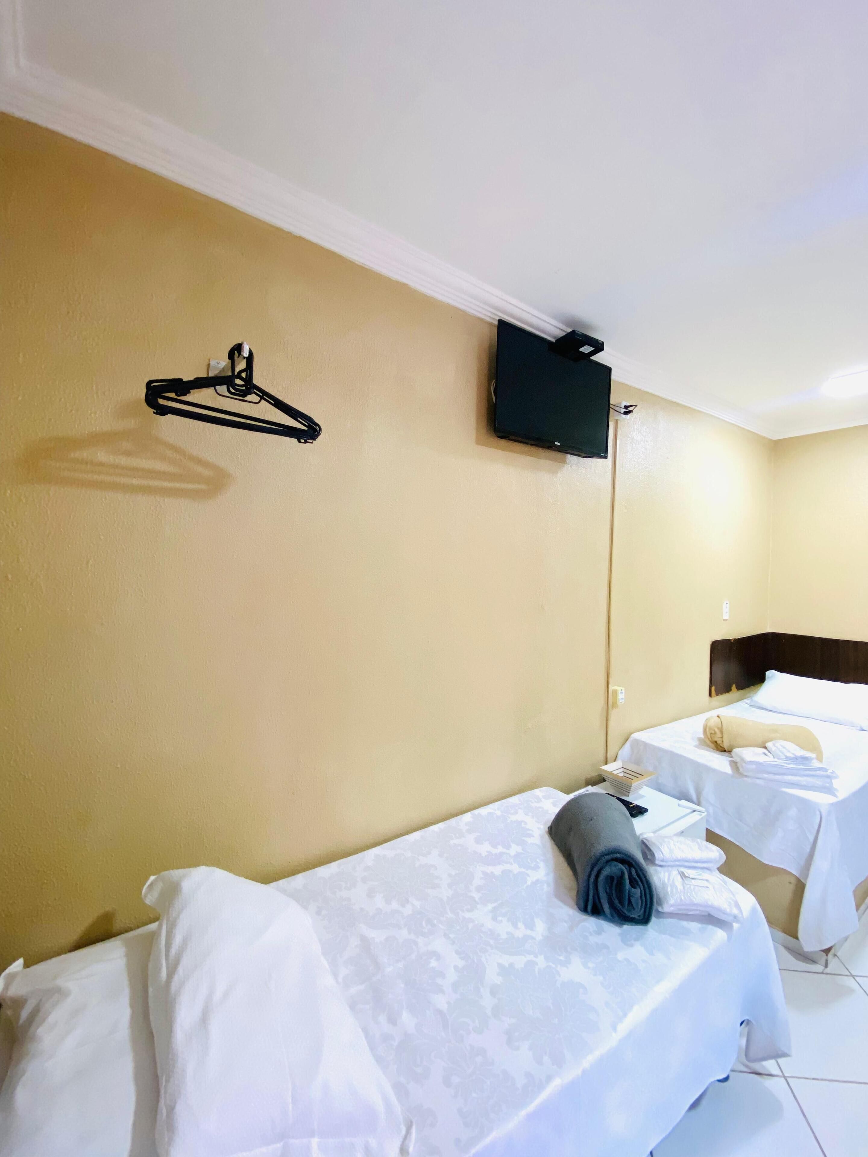Une chambre d’hôtel avec deux lits simples, un téléviseur fixé au mur et un porte-manteau.