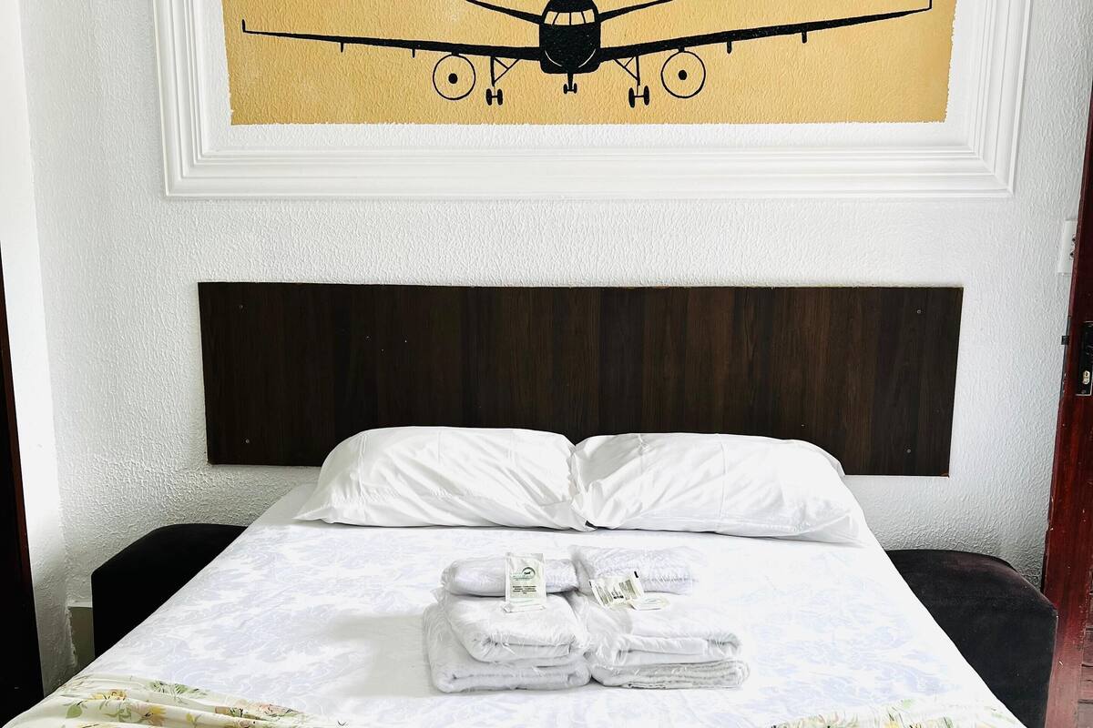 Une chambre d’hôtel avec un lit, une tête de lit, un tableau représentant un avion accroché au mur et une couvre-lit à motifs floraux.