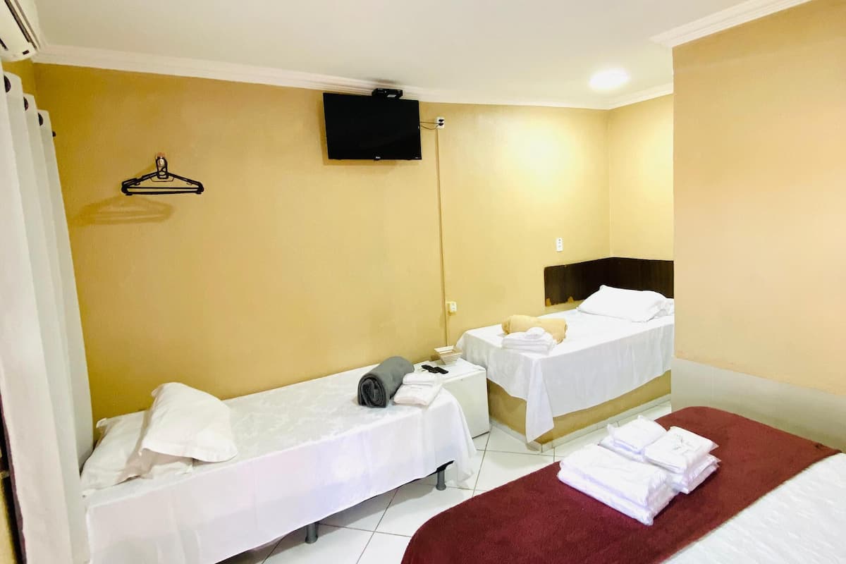Une chambre d’hôtel avec deux lits simples, un grand lit, un téléviseur fixé au mur et une moquette rouge.