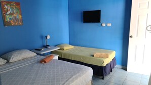 Una habitación con dos camas, un escritorio con lámpara, un televisor en la pared y una puerta.