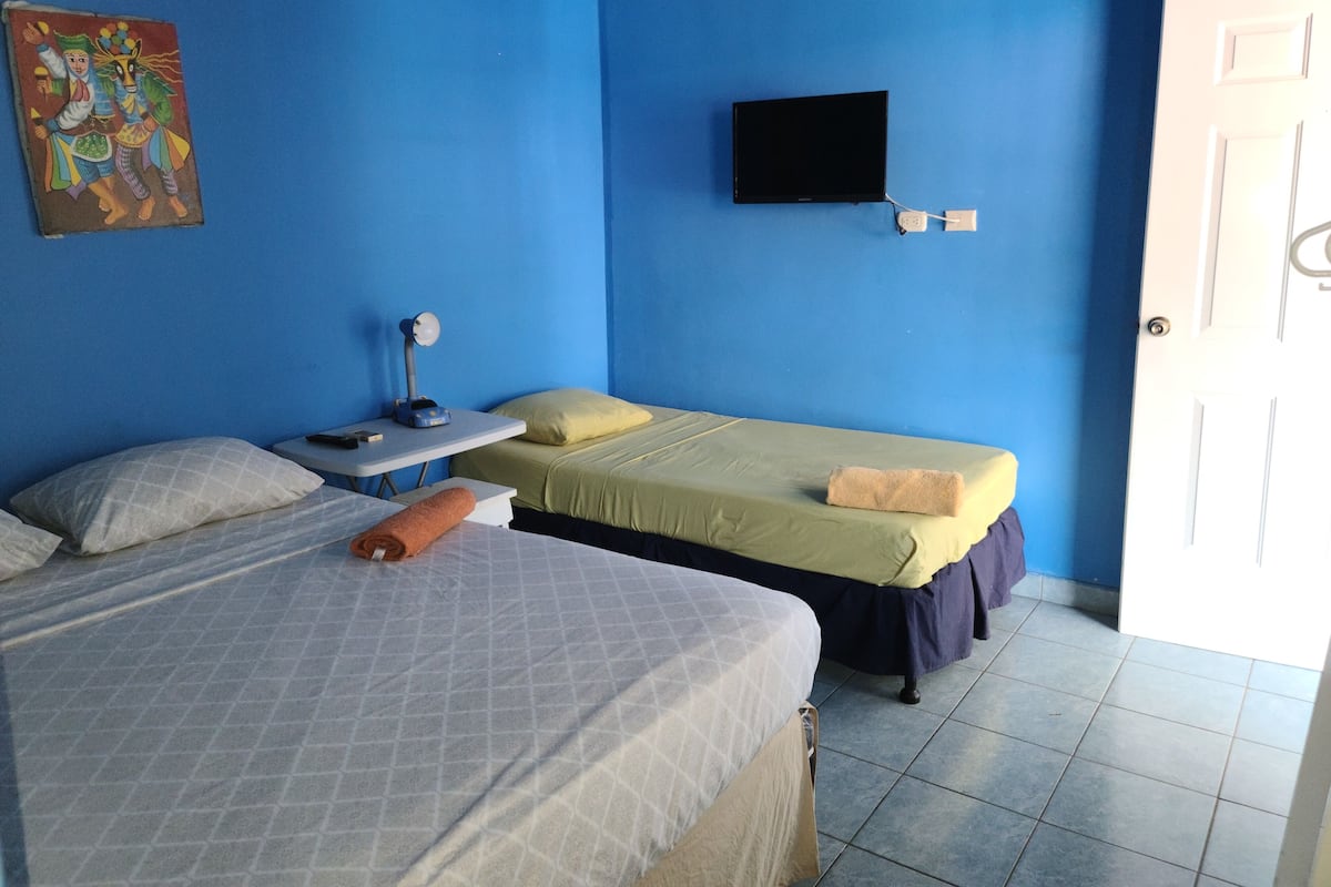 Una habitación con dos camas, un escritorio con lámpara, un televisor en la pared y una puerta.