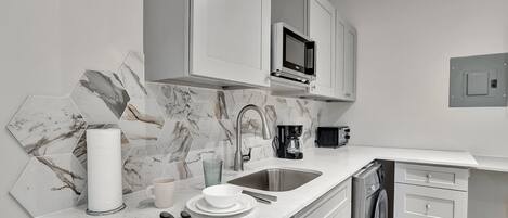Una cocina moderna con armarios blancos, un salpicadero de mármol, un microondas integrado y un lavavajillas.