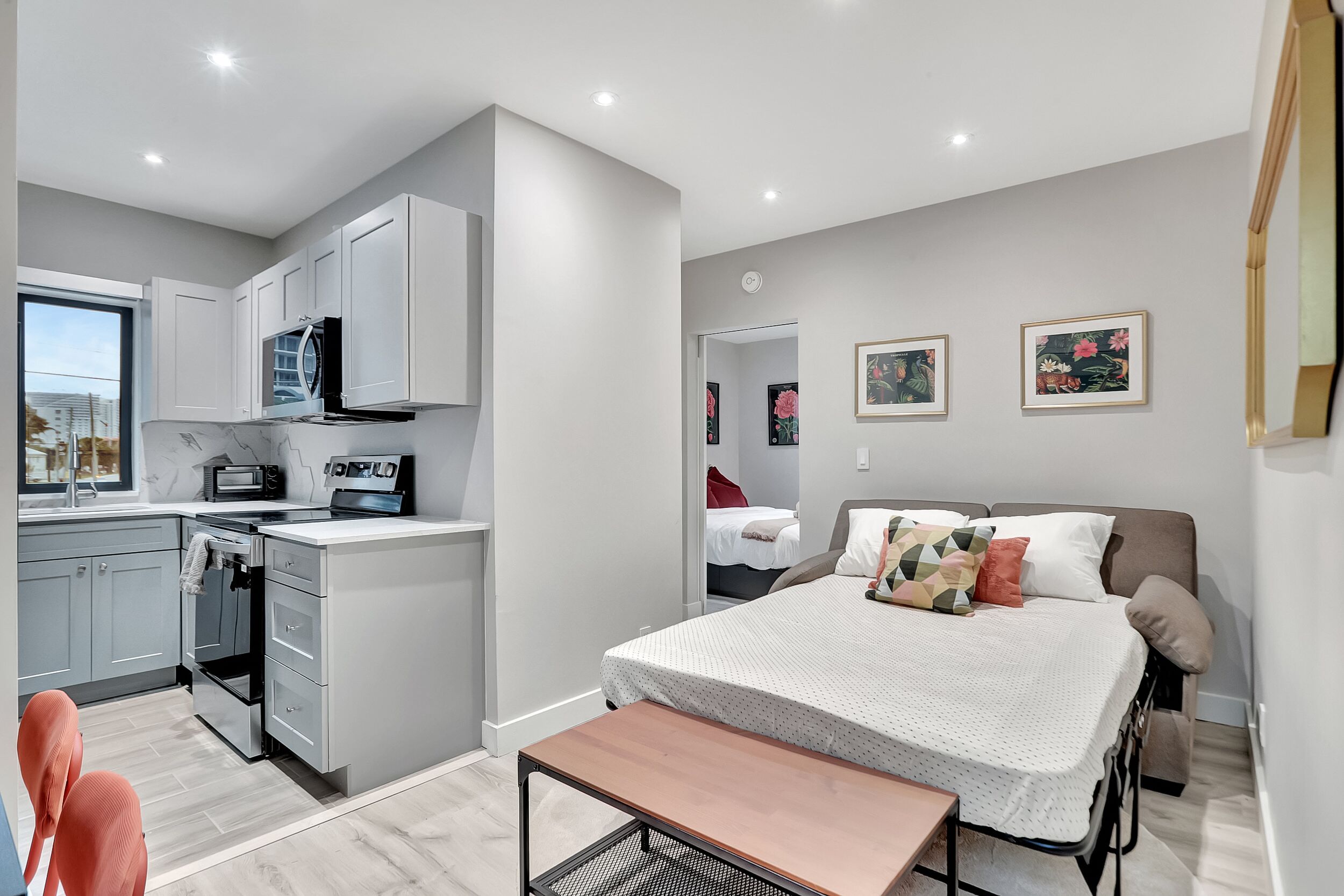 Un apartamento estudio compacto con kitchenette, una cama con muchos almohadones y una mesita.