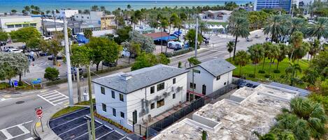 A white building with a flat roof, located near a street with palm trees and a view of the ocean.