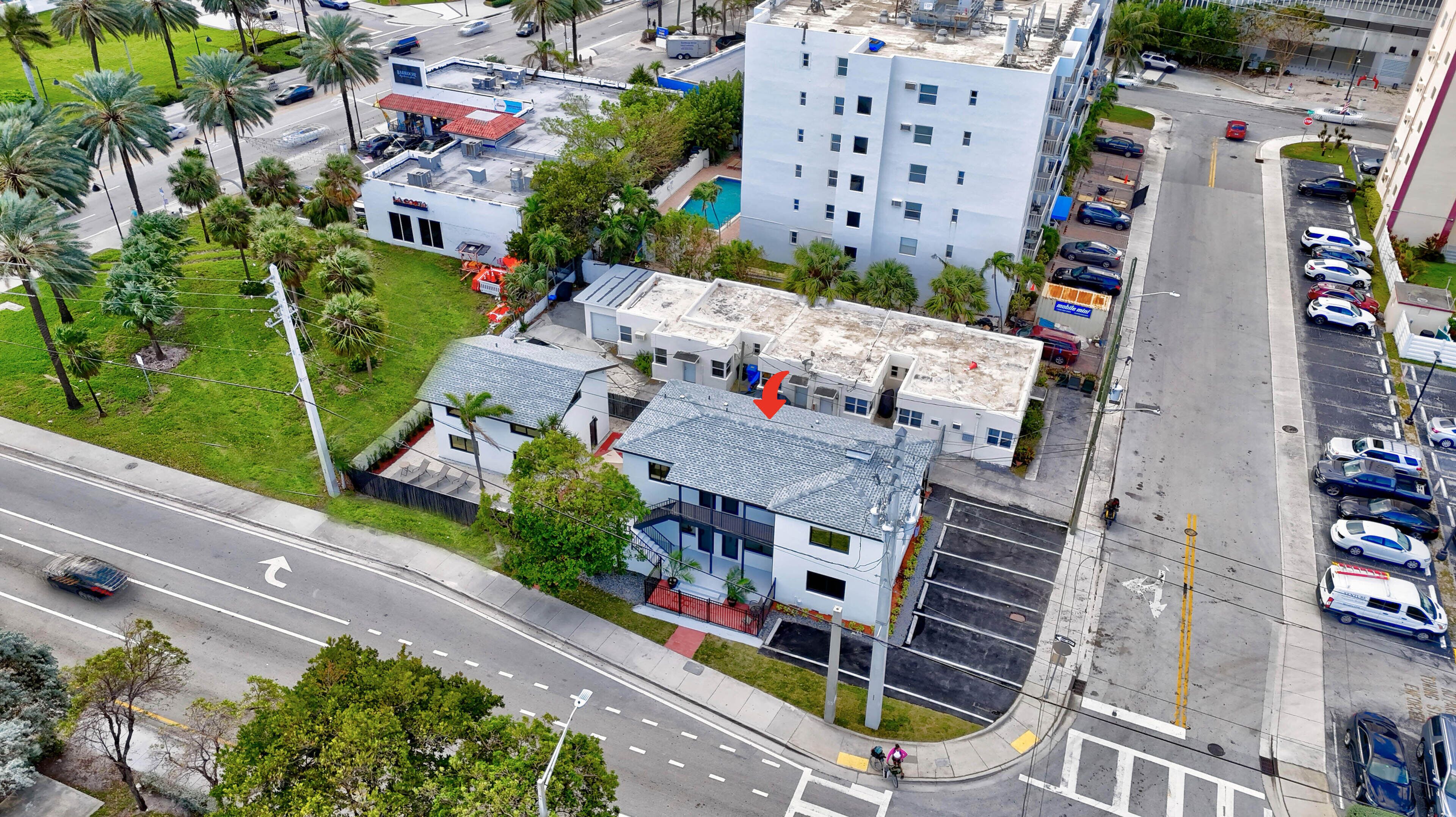 Eine Übersicht von oben eines Geschäftsgebäudes mit Parkplatz, neben einer Straße mit Autos und einer Fußgängerüberweg.
