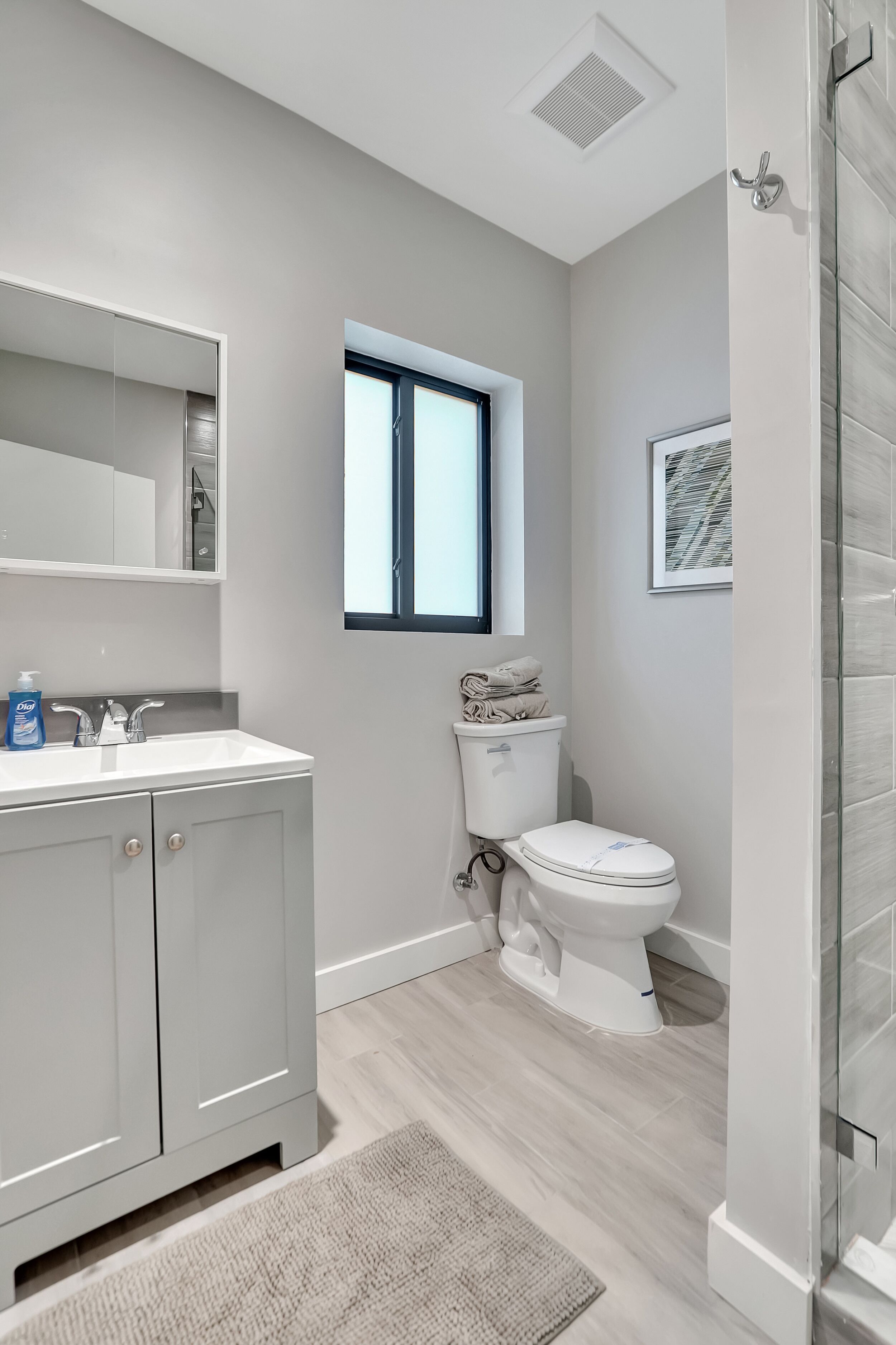 A modern bathroom with a white vanity, a toilet, a window, and a shower area.