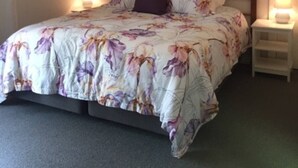 A bedroom with a floral bedspread, a wooden headboard, two bedside lamps, and a white nightstand. - Burradoo Loft with king size bed. 
Close to Southern Highlands wineries. (Burradoo)