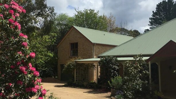 A two-story building with a green roof, surrounded by a well-maintained lawn and flowering plants. - Burradoo Loft with king size bed. 
Close to Southern Highlands wineries. (Burradoo)