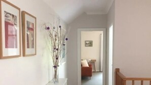 A hallway with wooden flooring, white walls, and a white console table with a vase of dried branches. There are framed pictures on the wall and a door leading to another room. - Burradoo Loft with king size bed. 
Close to Southern Highlands wineries. (Burradoo)