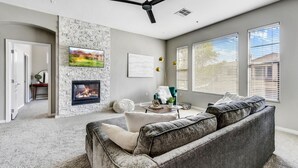 A living room with a fireplace, a ceiling fan, and a large window with blinds. - Cozy 2 Bed, 2 Bath in Grayhawk (Scottsdale)