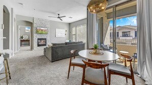 A modern living room with a fireplace, grey sofa, and a dining area with a round table and chairs. - Cozy 2 Bed, 2 Bath in Grayhawk (Scottsdale)
