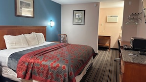A hotel room with a bed, a chair, a desk with a computer, and a microwave.