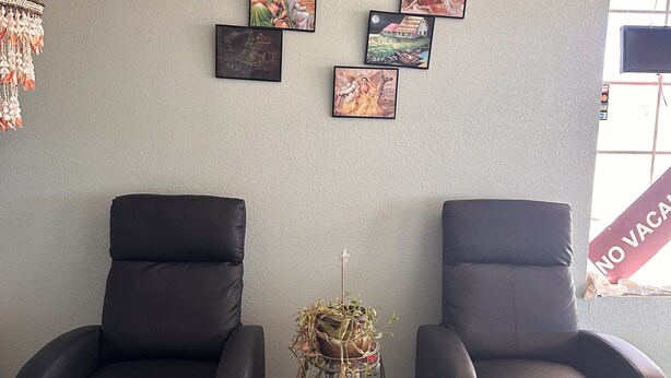 A room with two black leather chairs, a wall decorated with framed pictures, and a small table with a plant.